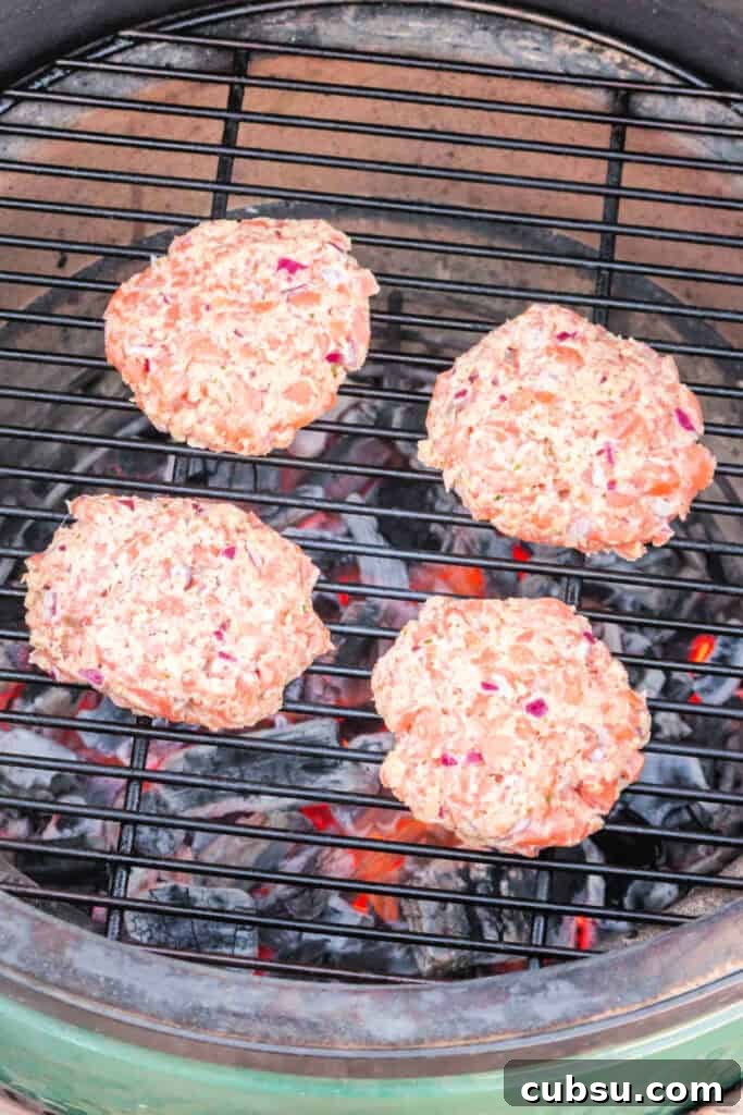 Raw salmon burger patties placed on a hot grill with visible coals