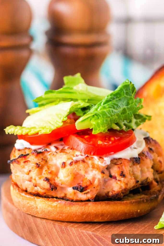 Close-up of a fully assembled grilled salmon burger with lettuce and tomato