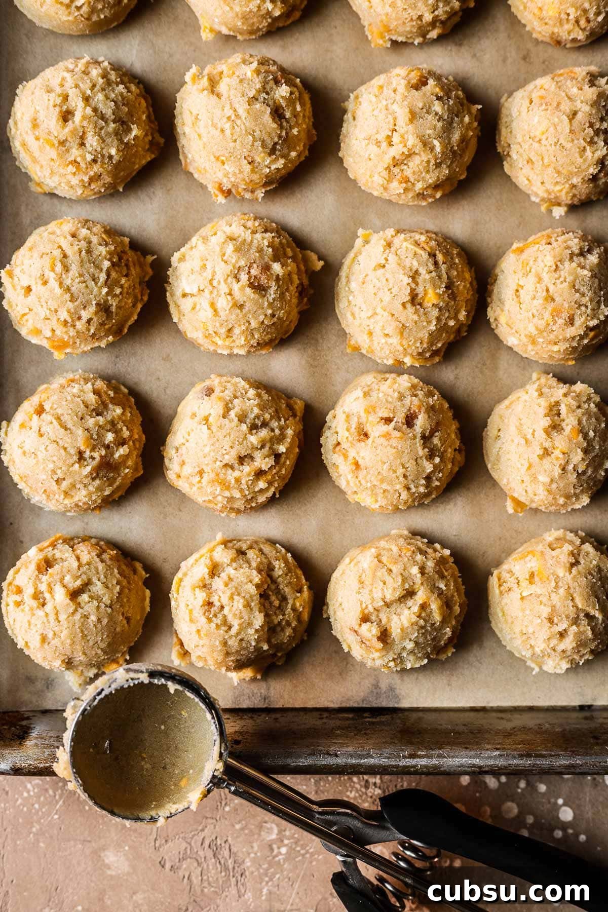 Scoops of mango cookie dough on a parchment lined baking sheet.