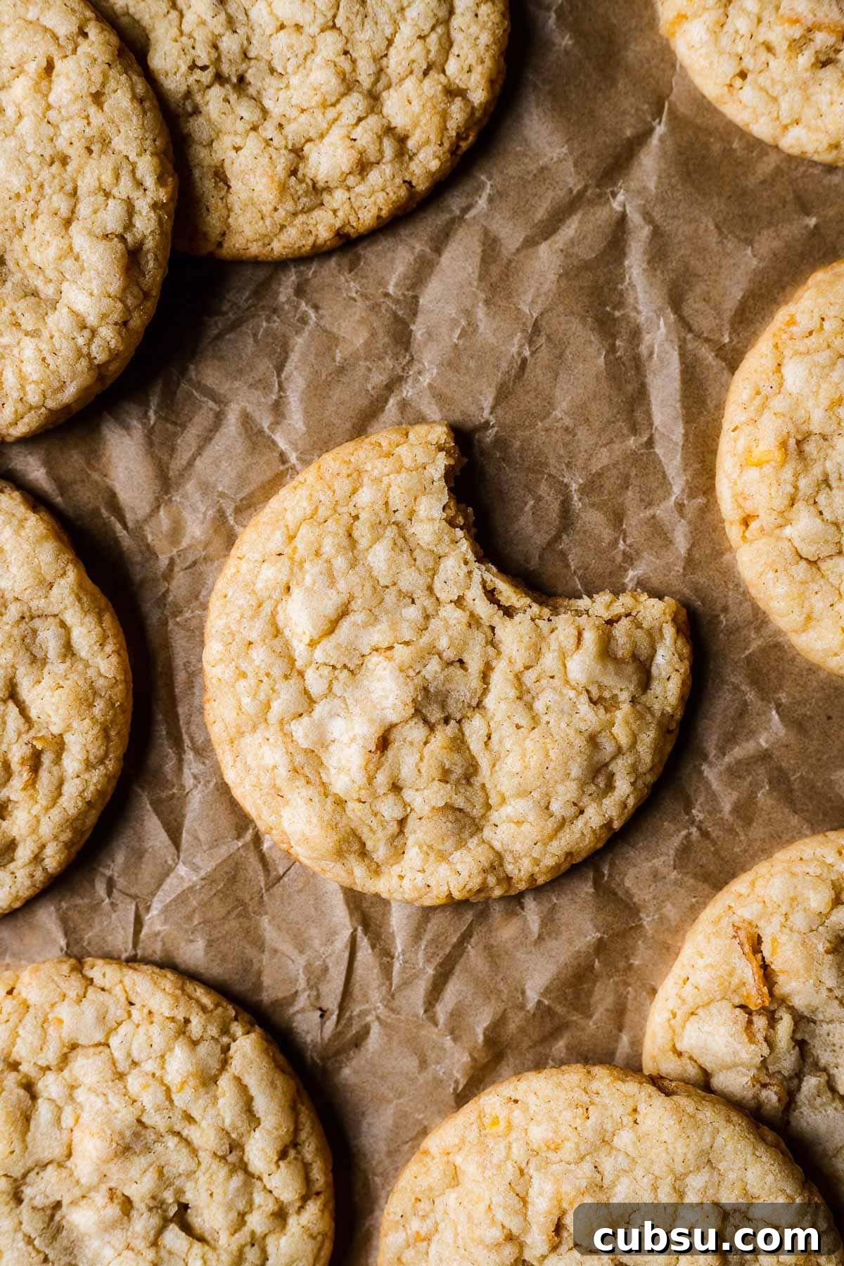 A cookie on brown parchmenet with one bite taken out of it. More cookies peek into the frame.