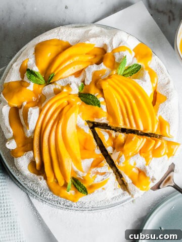 A coconut cake with baked meringue is decorated with vibrant yellow mango slices and mango puree.
