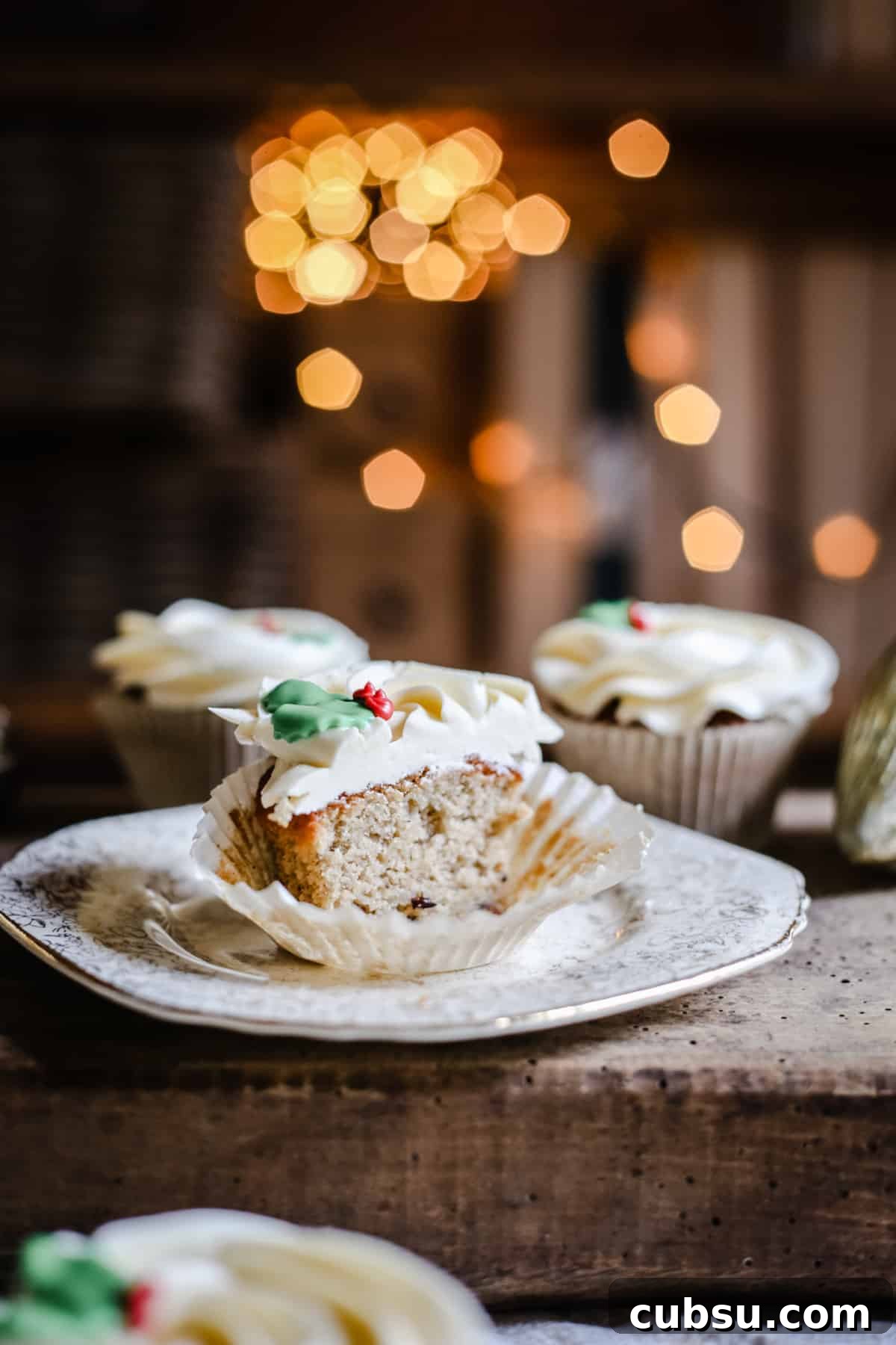 Mince Pie Cupcakes, sliced in half on a plate on a wooden board surrounded by cupcakes and twinkling lights