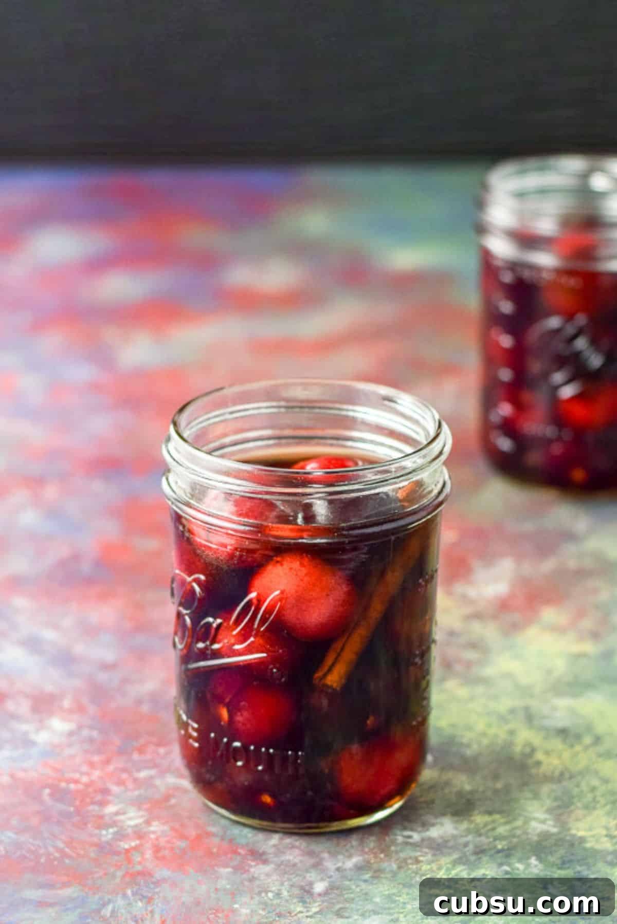 Cherries and cinnamon in bourbon in two jars on a table