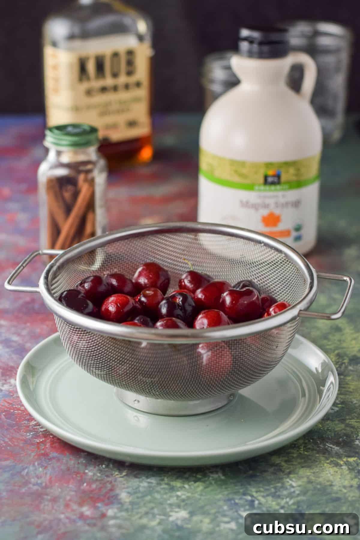 Cherries, cinnamon sticks, bourbon and maple syrup on a colorful table
