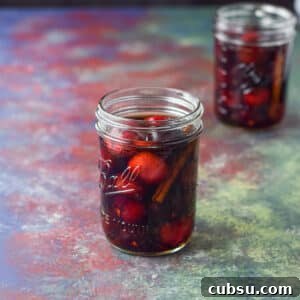 Cherries and cinnamon in bourbon in two jars on a table - square