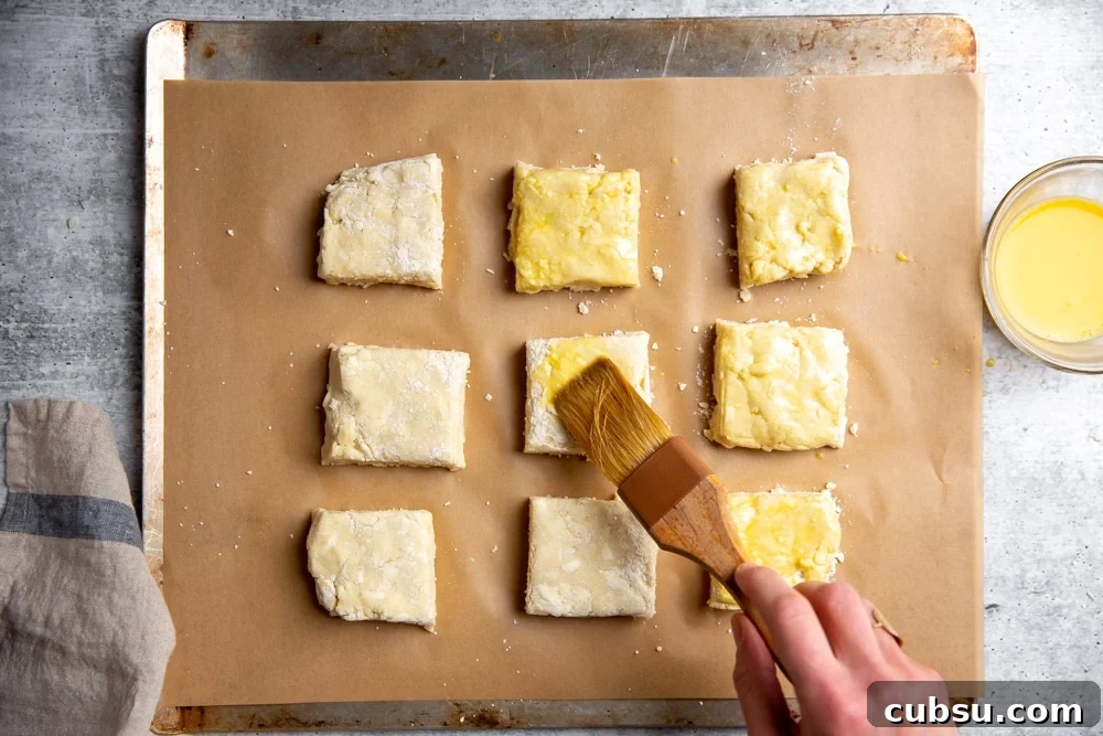 Process shot showing a hand brushing the shortcakes with egg wash. 