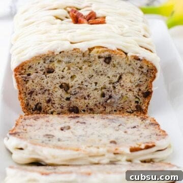 A cross section of a loaf of buttermilk banana bread with cream cheese frosting drizzled on the top.