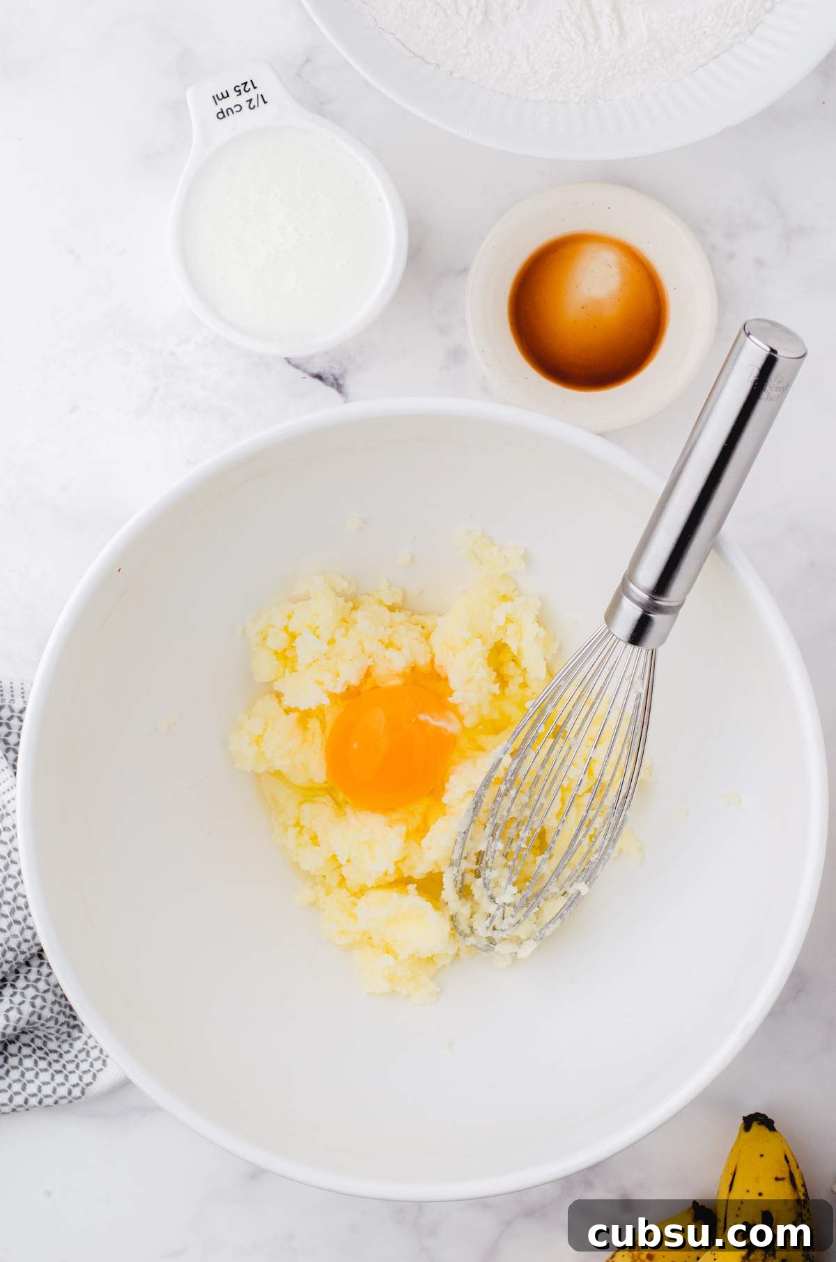 A white bowl of butter, eggs, and sugar for buttermilk banana bread.