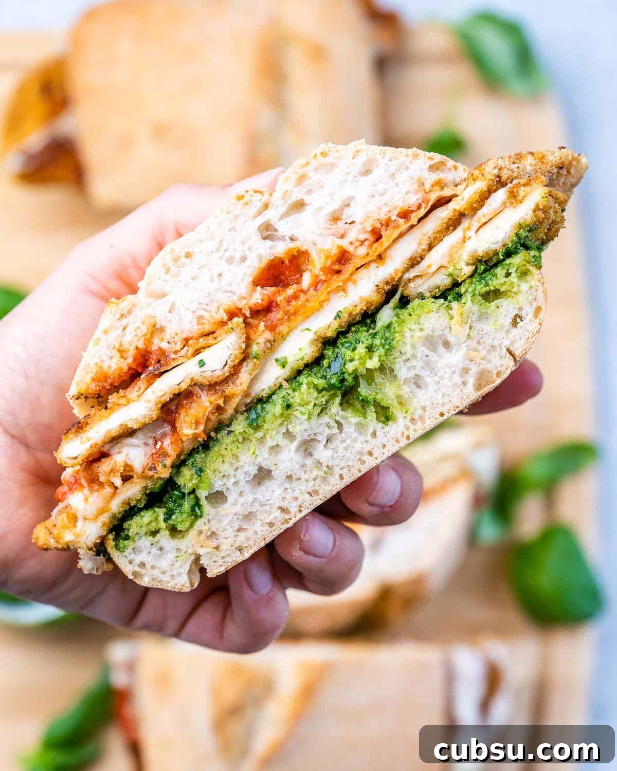 Crispy Chicken Parmesan Sandwich Recipe That Beats Takeout 2 Another hand-held shot of the sandwich with breaded chicken and pesto clearly visible between the toasted bread layers.