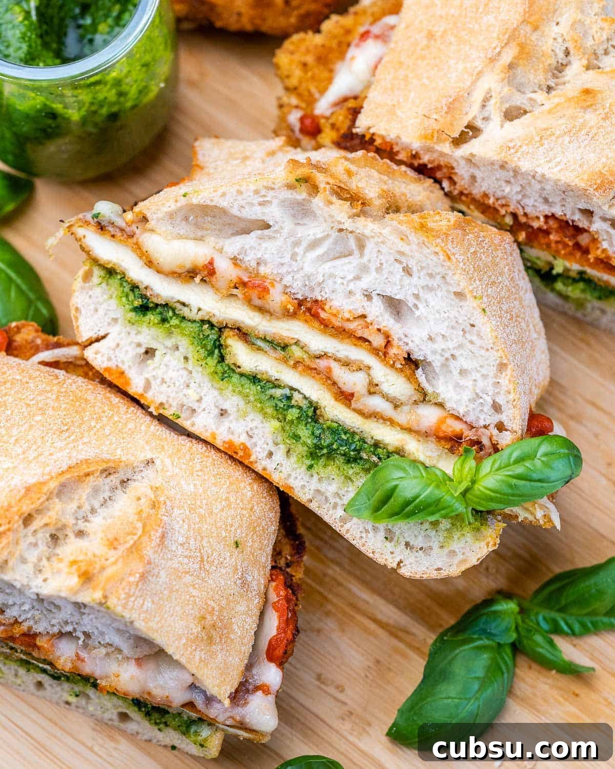 Crispy Chicken Parmesan Sandwich Recipe That Beats Takeout 6 Sandwich halves filled with breaded chicken, pesto, marinara, and mozzarella, layered inside toasted ciabatta rolls with basil garnish.