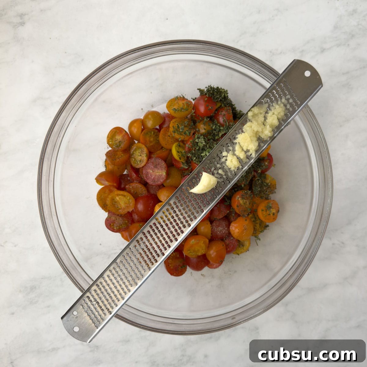 Zesting garlic fine into a bowl of cherry tomatoes for roasting.