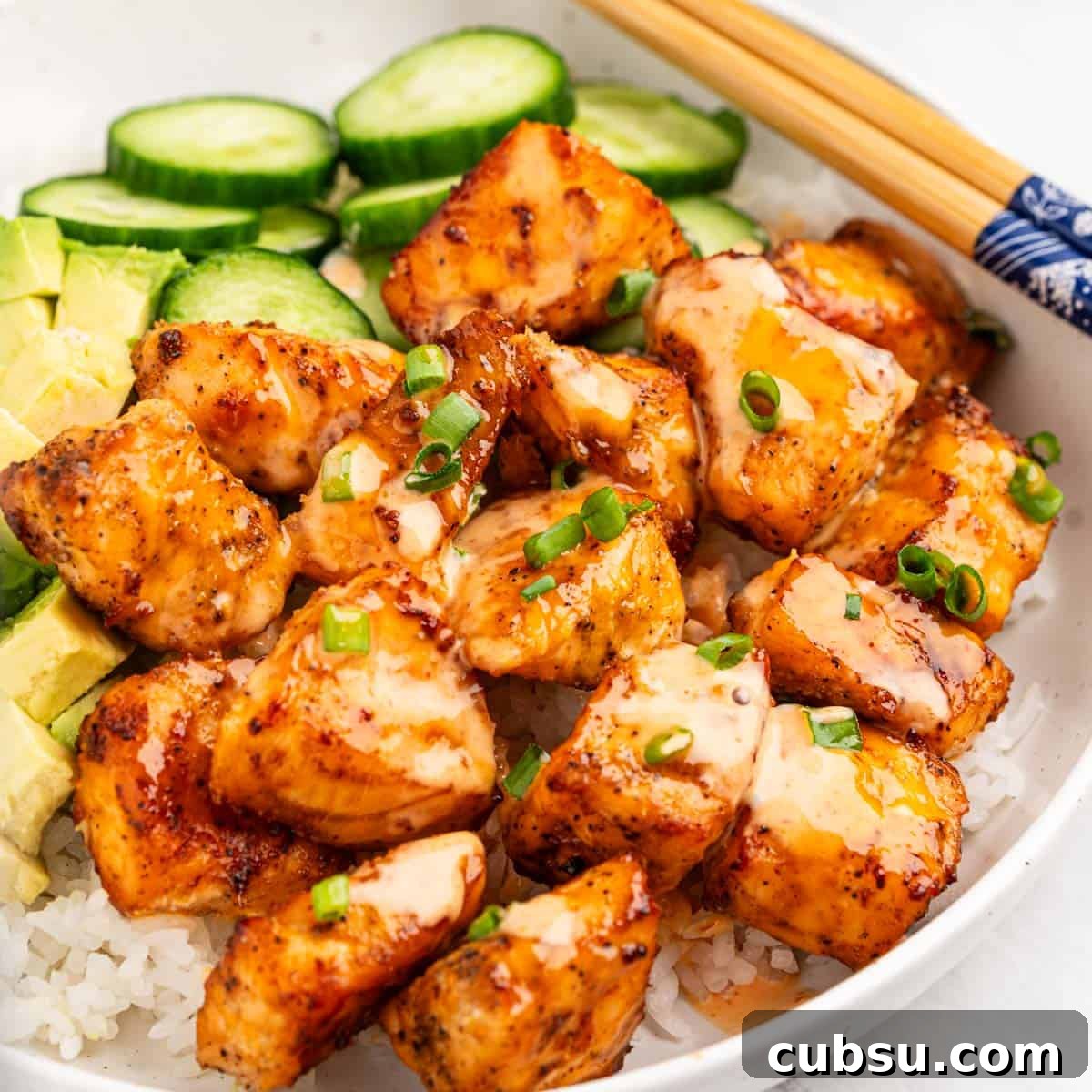 plate of air fryer salmon bites on bed of rice with slices of cucumbers and avocado.