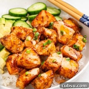 plate of air fryer salmon bites on bed of rice with slices of cucumbers and avocado.