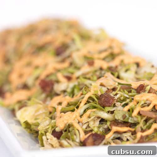 white plate of shaved brussels sprouts with spicy mayo drizzled on top