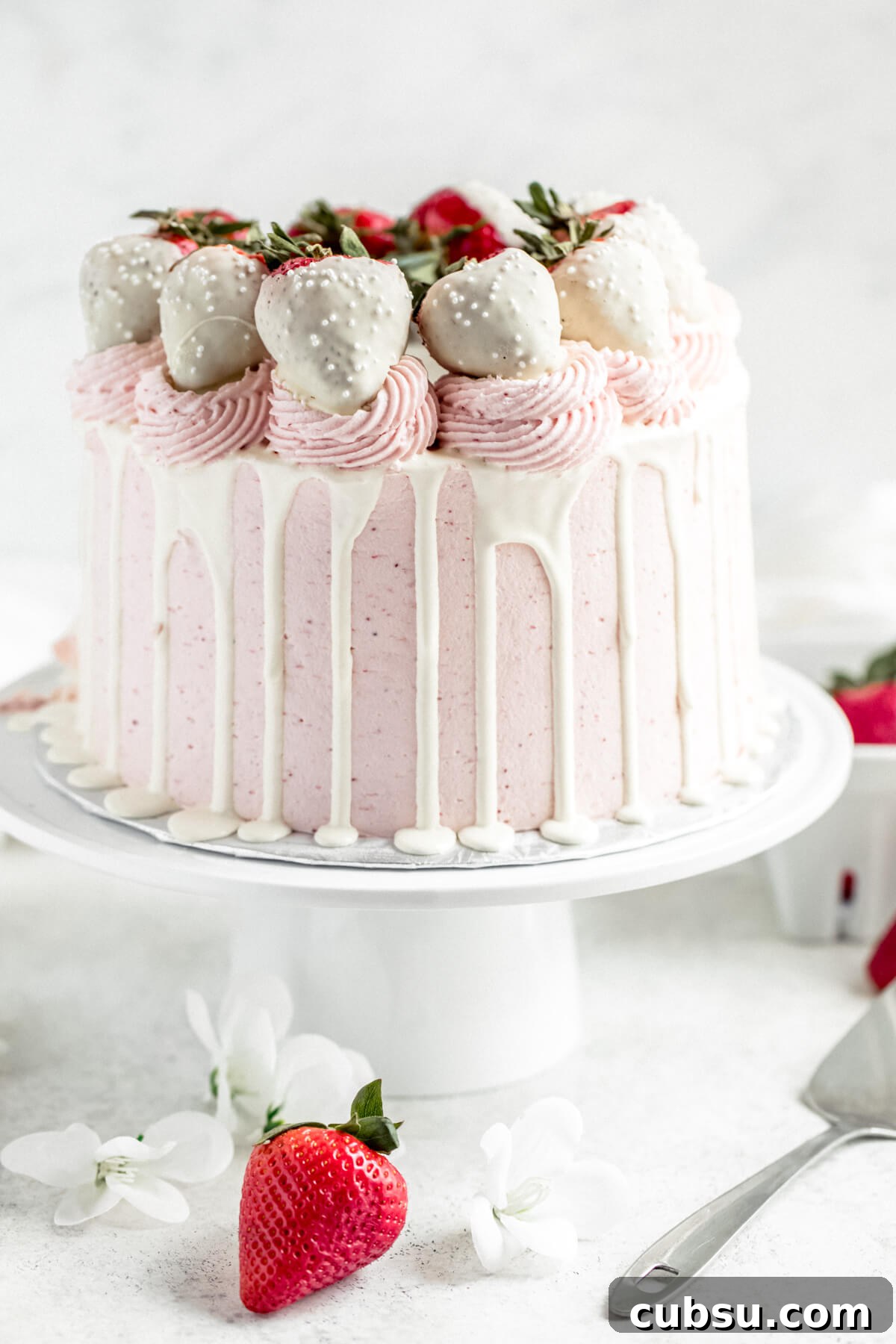strawberry and white chocolate cake on a cake stand with strawberries in the background