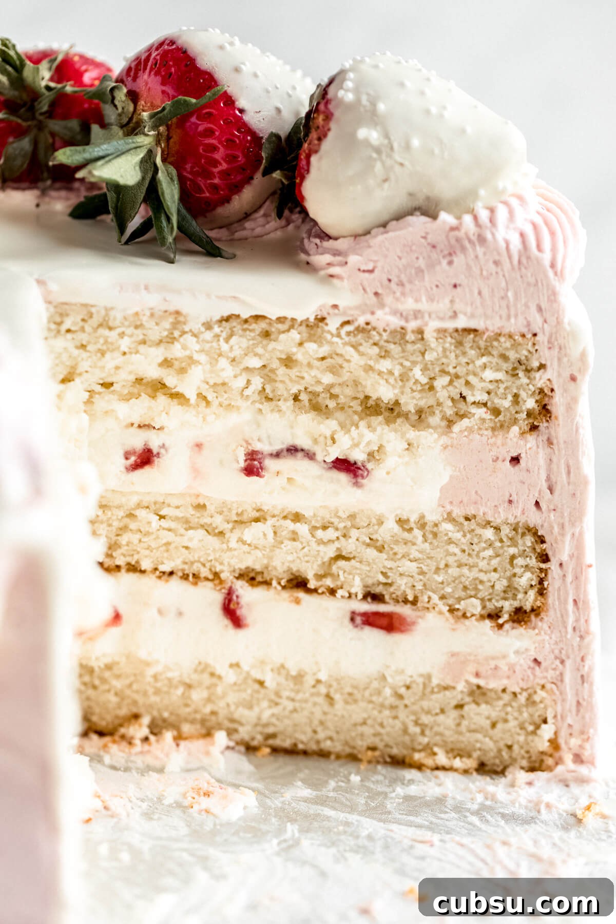 cut open cake on a cake stand with white chocolate mousse and strawberries inside