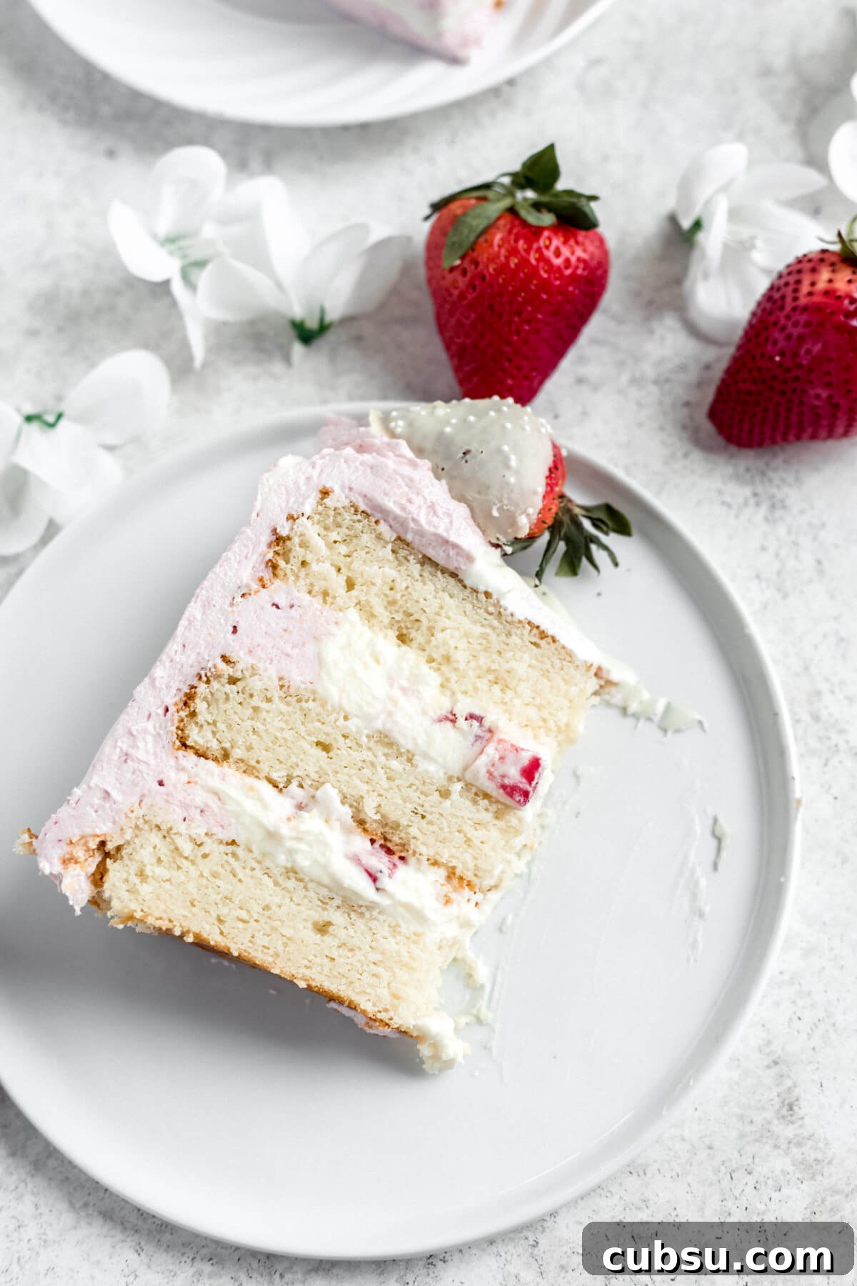 slice of white cake with mousse filling on a white plate with strawberries beside