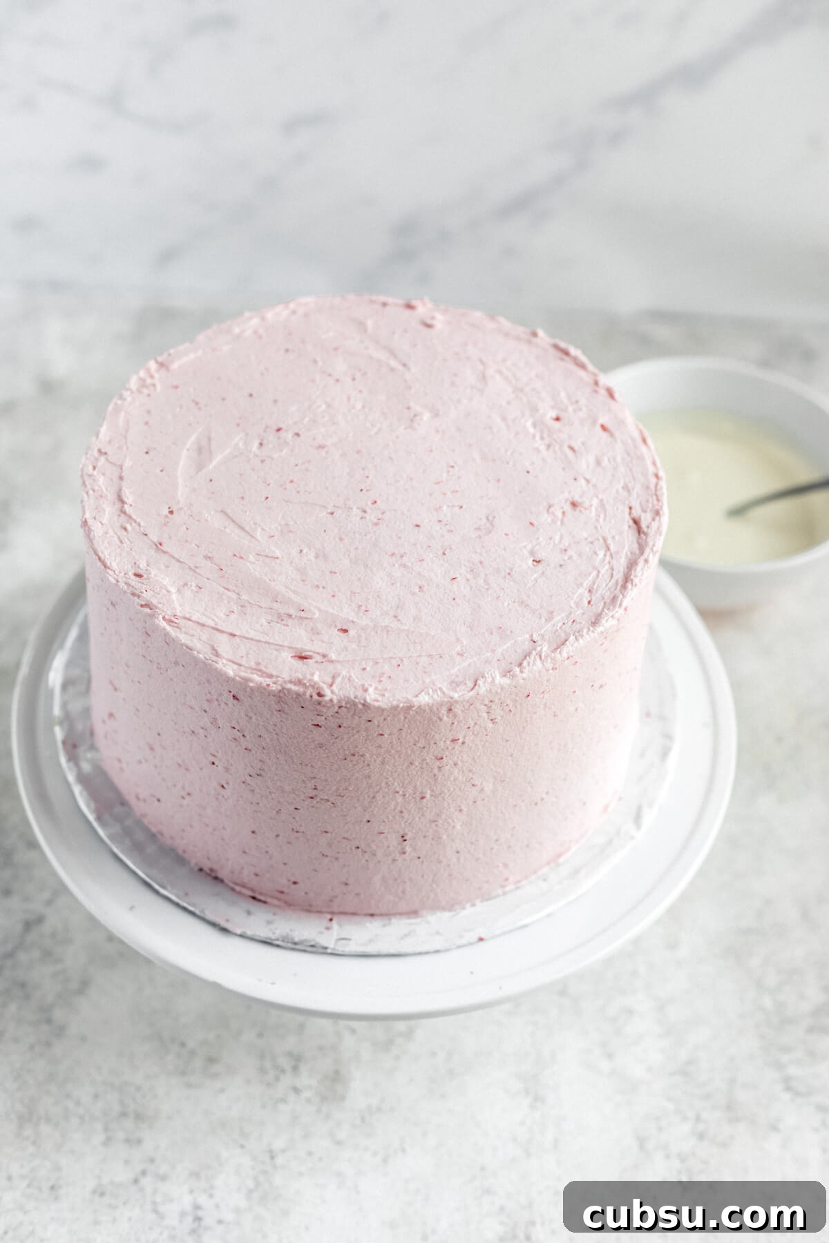 frosted cake on a cake stand with white chocolate ganache in the background