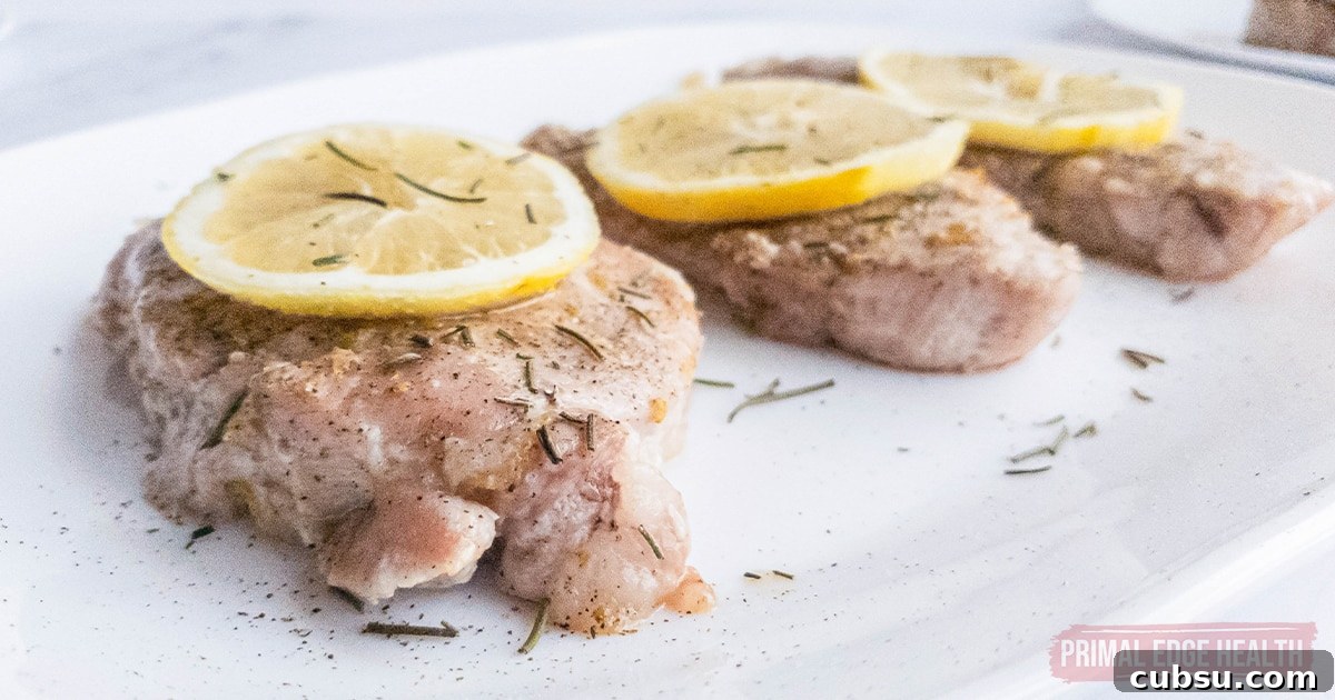 Three pork chops with seasoning and lemon slice on top.