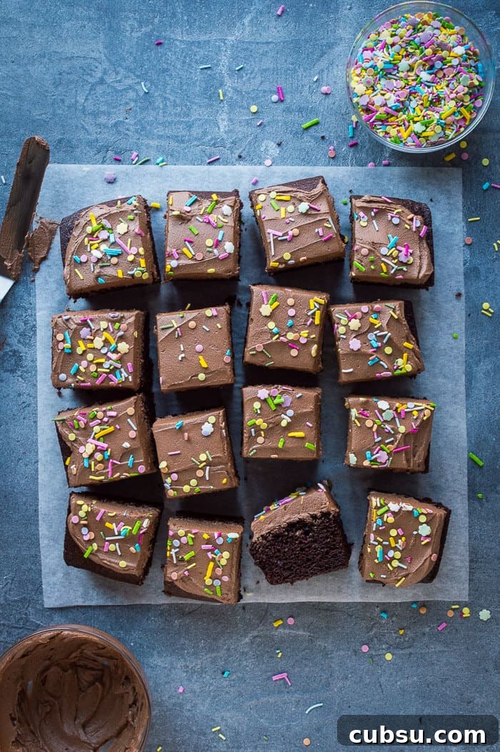 Decadent Vegan Chocolate Cake Recipe: Moist, Dairy-Free Slice 8 Easy vegan chocolate cake sliced into squares on a grey background with a bowl of sprinkles and a bowl of buttercream.