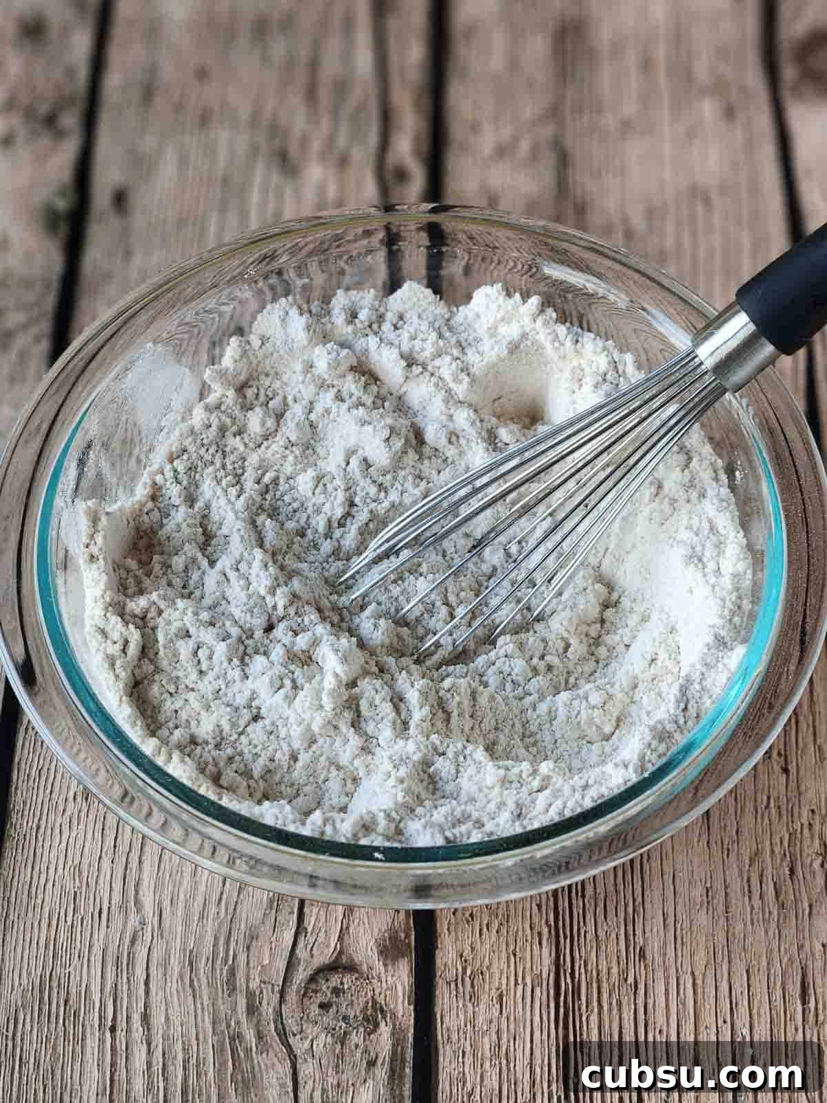 Dry ingredients in a clear bowl with a whisk in it.