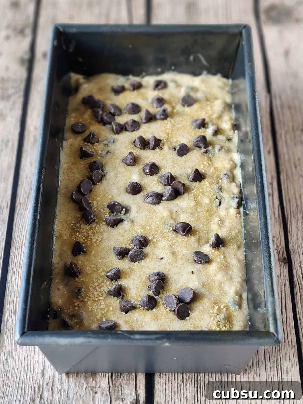 Prepared batter in a metal loaf pan on a wood surface.