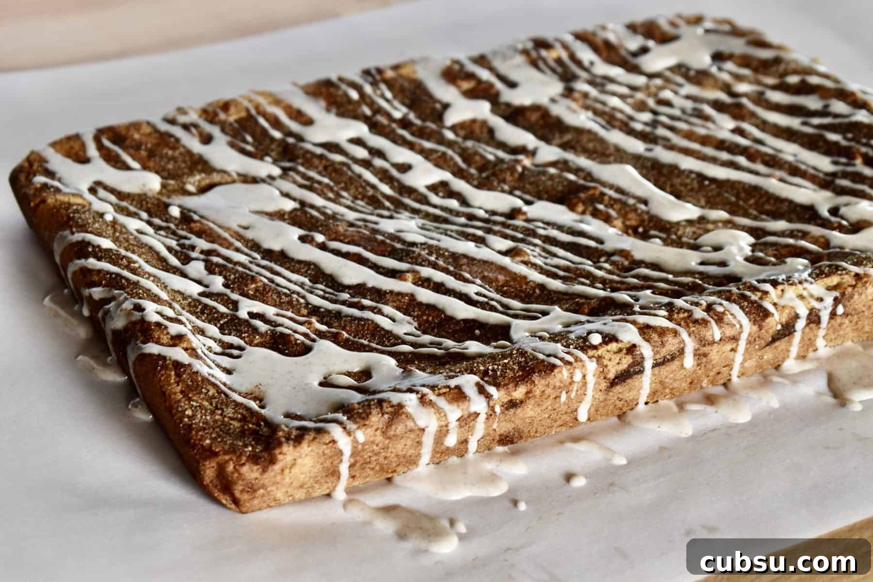 Chewy Cinnamon Sugar Blondies Recipe for Perfect Texture 10 glaze drizzled over the top of the cinnamon sugar blondies on a piece of parchment paper.