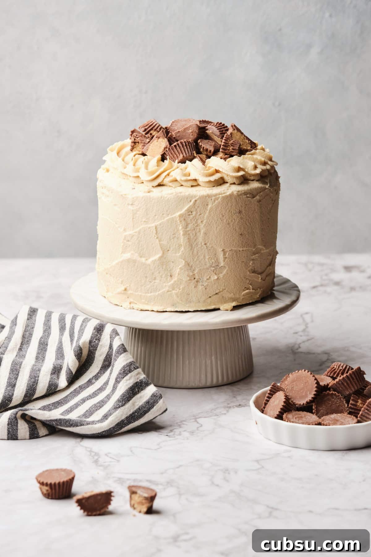 Chocolate Cake with Creamy Peanut Butter Frosting Recipe 12 A Peanut Butter Chocolate Cake on a pedestal near some peanut butter cups,
