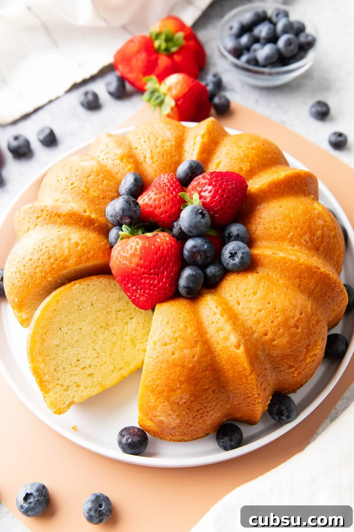 Classic Buttermilk Pound Cake Recipe with Tender Crumb 2 Buttermilk pound cake on a serving platter with berries and one slice sitting on the platter.