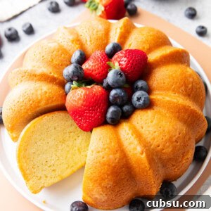 Classic Buttermilk Pound Cake Recipe with Tender Crumb 10 Buttermilk pound cake on a serving platter with berries and one slice sitting on the platter.