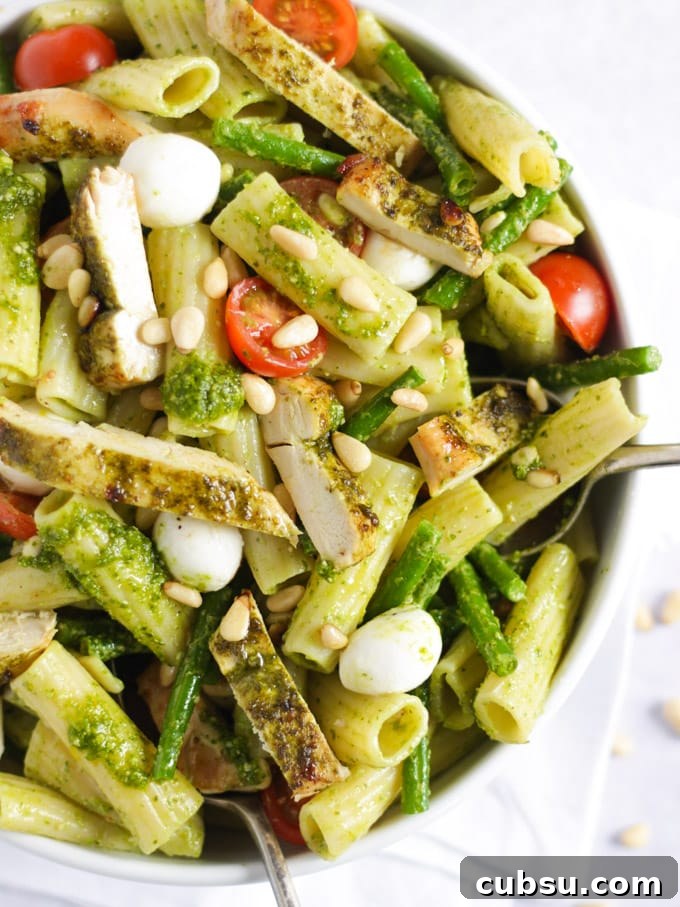 White bowl of Chicken pesto pasta with tomatoes, mozzarella cheese and green beans