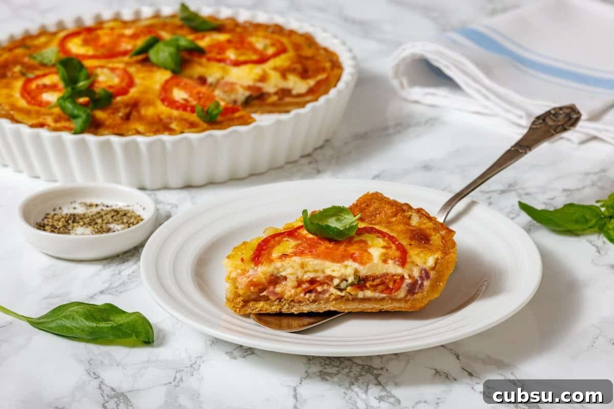 31 Classic Comfort Recipes That Keep Families Coming Back 13 A slice of tomato pie on a white plate with a serving utensil, and a whole tomato pie in a white fluted dish, are shown on a marble surface with a small bowl of spices and basil leaves.