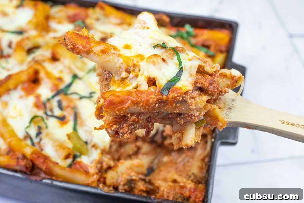 31 Classic Comfort Recipes That Keep Families Coming Back 18 A close-up of a wooden spoon lifting a serving of baked ziti with melted cheese and tomato sauce from a casserole dish.