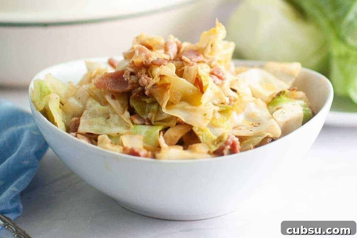 31 Classic Comfort Recipes That Keep Families Coming Back 20 A white bowl filled with fried cabbage with pieces of bacon sits on a white surface with a blue cloth nearby.