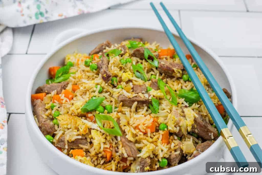 31 Classic Comfort Recipes That Keep Families Coming Back 3 A bowl of steak fried rice served with blue chopsticks on a white tiled surface.