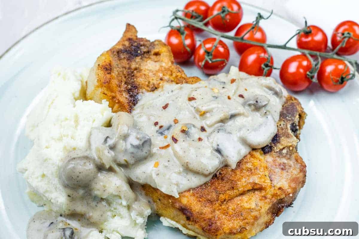 31 Classic Comfort Recipes That Keep Families Coming Back 21 Plate with Cast Iron Smothered Pork Chops served alongside mashed potatoes and vine tomatoes.