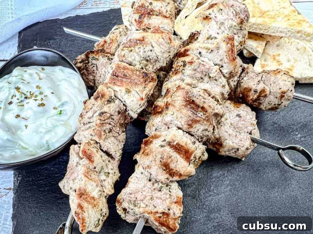 31 Classic Comfort Recipes That Keep Families Coming Back 28 Three pieces of Pork Souvlaki with a bowl of white sauce and pieces of flatbread on a black slate serving board.