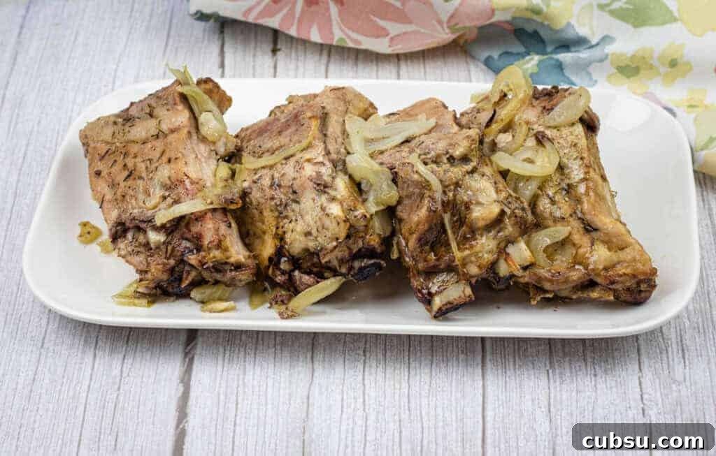 31 Classic Comfort Recipes That Keep Families Coming Back 4 Oven-baked ribs with onion and garlic on top served on a white rectangular plate.