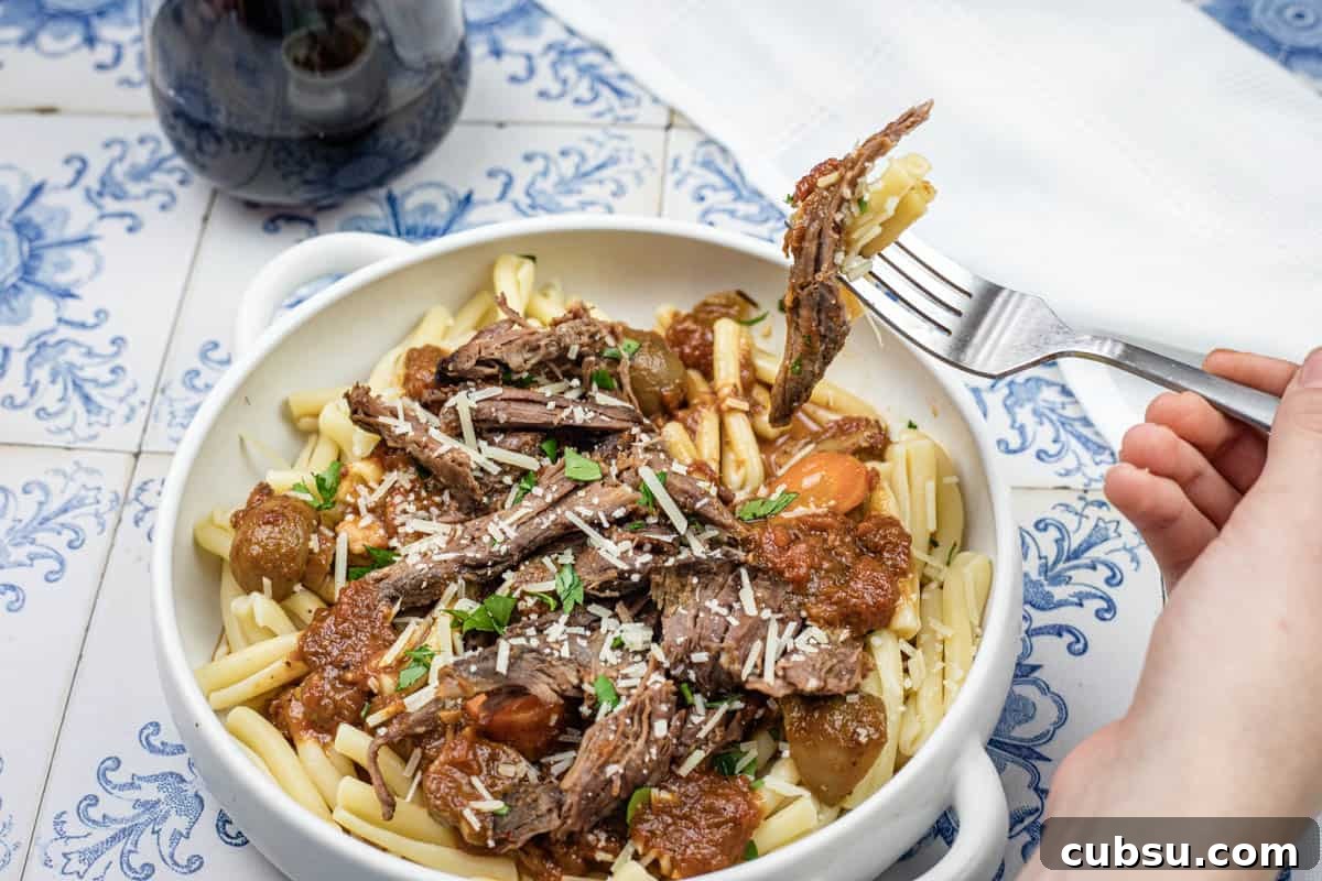 31 Classic Comfort Recipes That Keep Families Coming Back 31 A hand lifting a fork with a bite of Italian Pot Roast Pasta on a bowl.