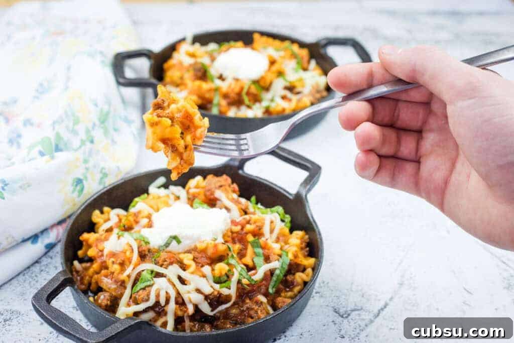 31 Classic Comfort Recipes That Keep Families Coming Back 5 A hand holds a fork with a Classic Skillet Lasagna with Ground Beef topped with melted cheese and herbs.