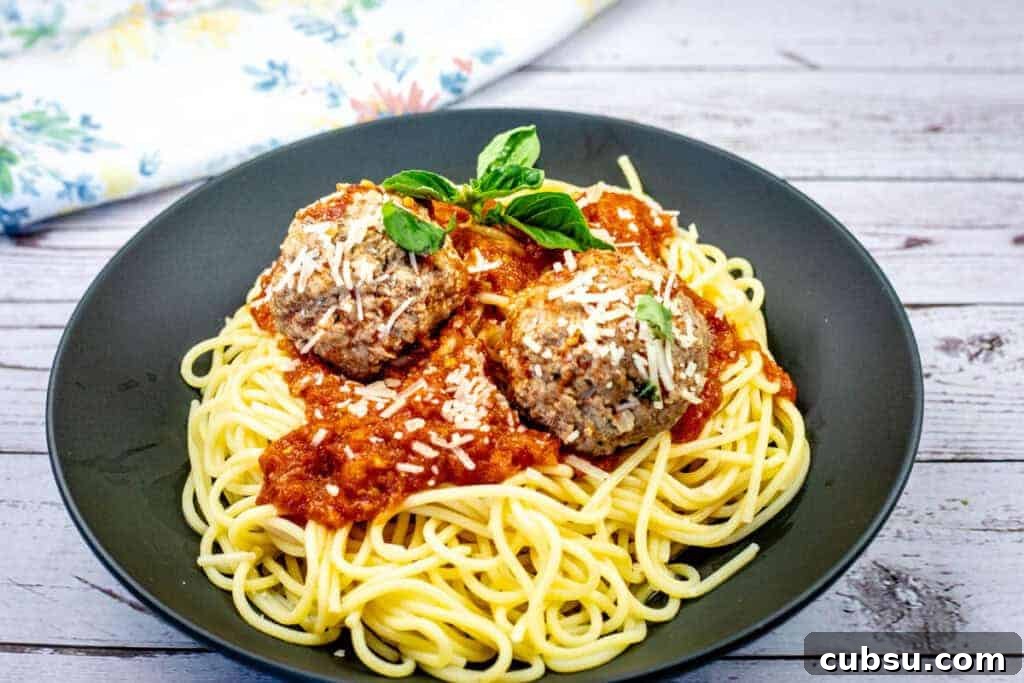 31 Classic Comfort Recipes That Keep Families Coming Back 10 A plate of spaghetti topped with two meatballs, marinara sauce, grated cheese, and basil garnish.