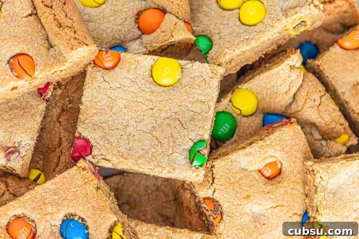 M&M Blondies Recipe: Chewy Chocolate Candy Bar Blondies 3 A pile of blondies with M&Ms.