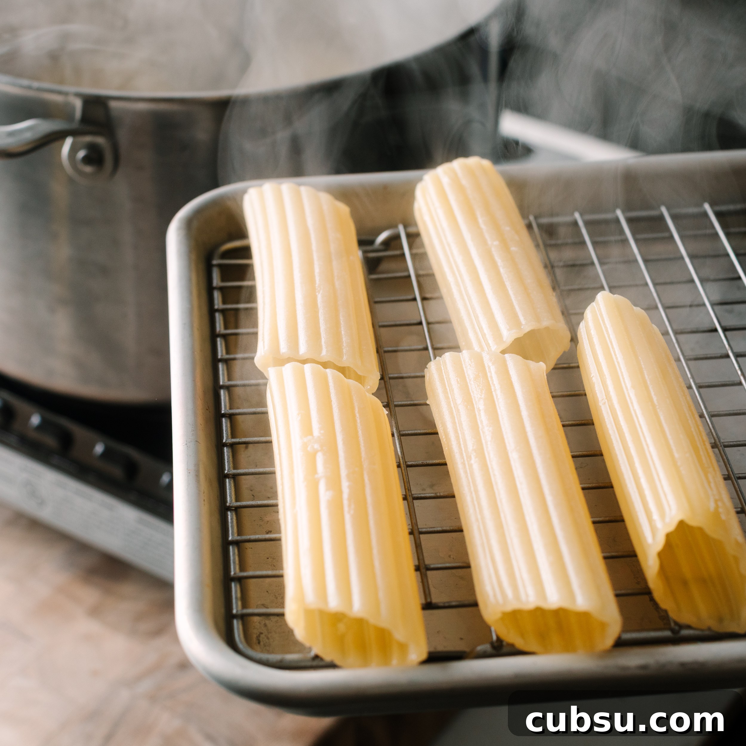Smoked Shotgun Shells: How They're Made and What to Know 4 Cannelloni shells on a wire rack set over a sheet pan with a pot of boiling water in the background.