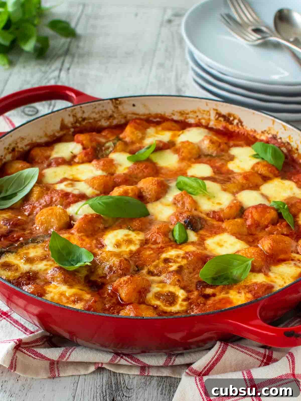 Gnocchi alla Sorrentina in a round red pan with plate in the background.