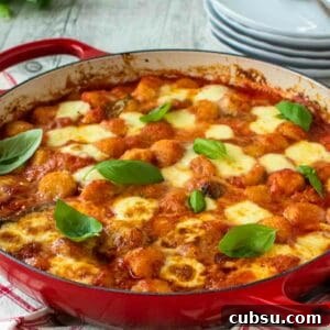 Gnocchi alla sorrentina in a round red pan with plate in the background.