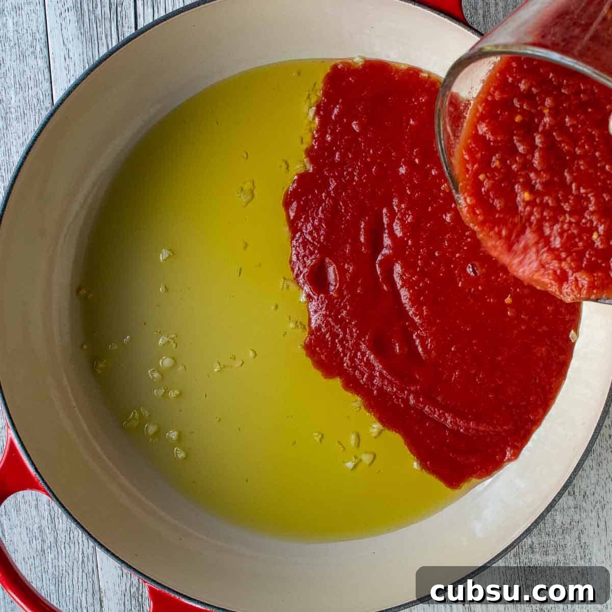 Tomato puree being poured into oil and chopped garlic.