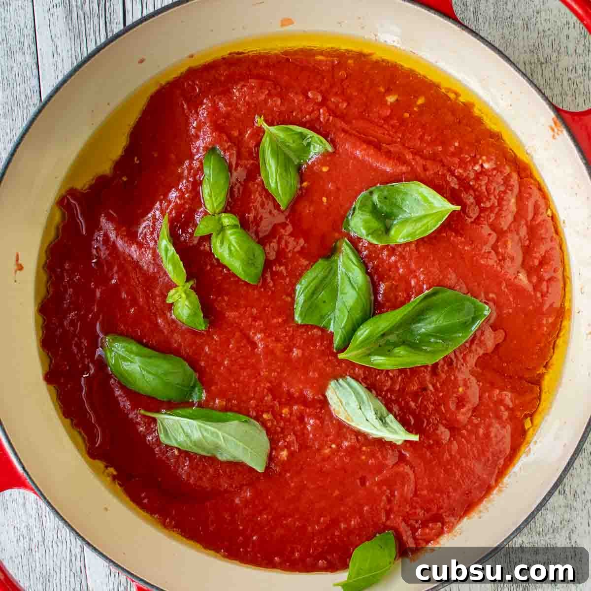 Overhead view of fresh basil leaves on top of tomato sauce in a pan.