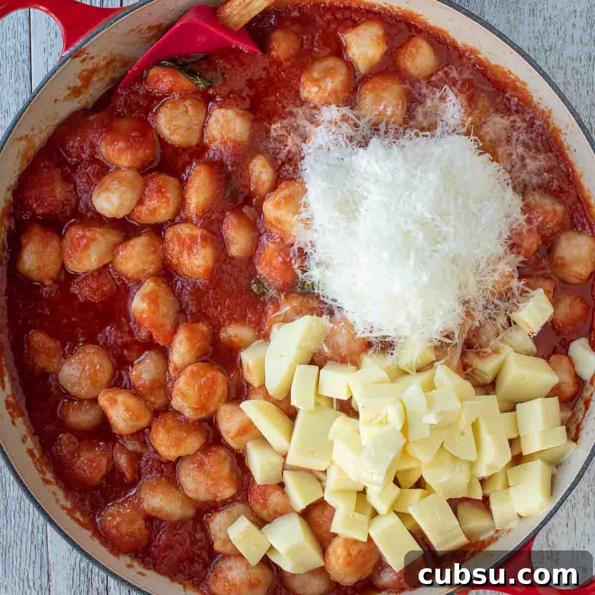 Overhead view of gnocchi in tomato sauce topped with piles of grated Parmesan cheese and cubes of mozzarella cheese.