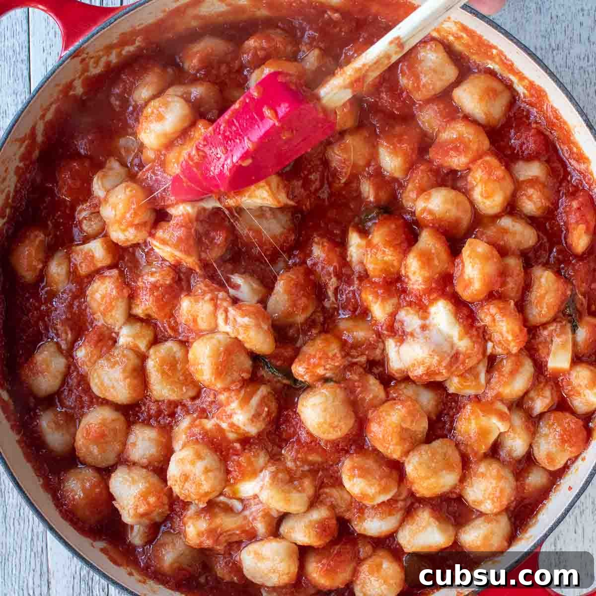 Overhead view of gnocchi in tomato sauce and cheese pulling strings.