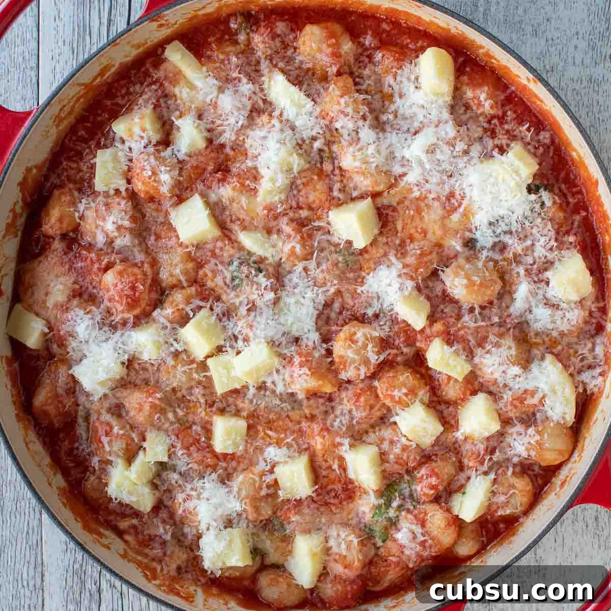 Overhead view of cubes of cheese and finely grated cheese sprinkled over tomato sauce covered pasta.